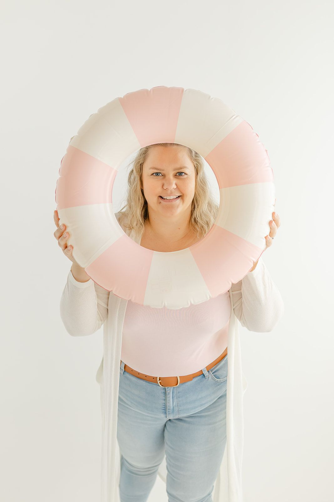 Image of a woman holding a camera and smiling, with a pink and white background.