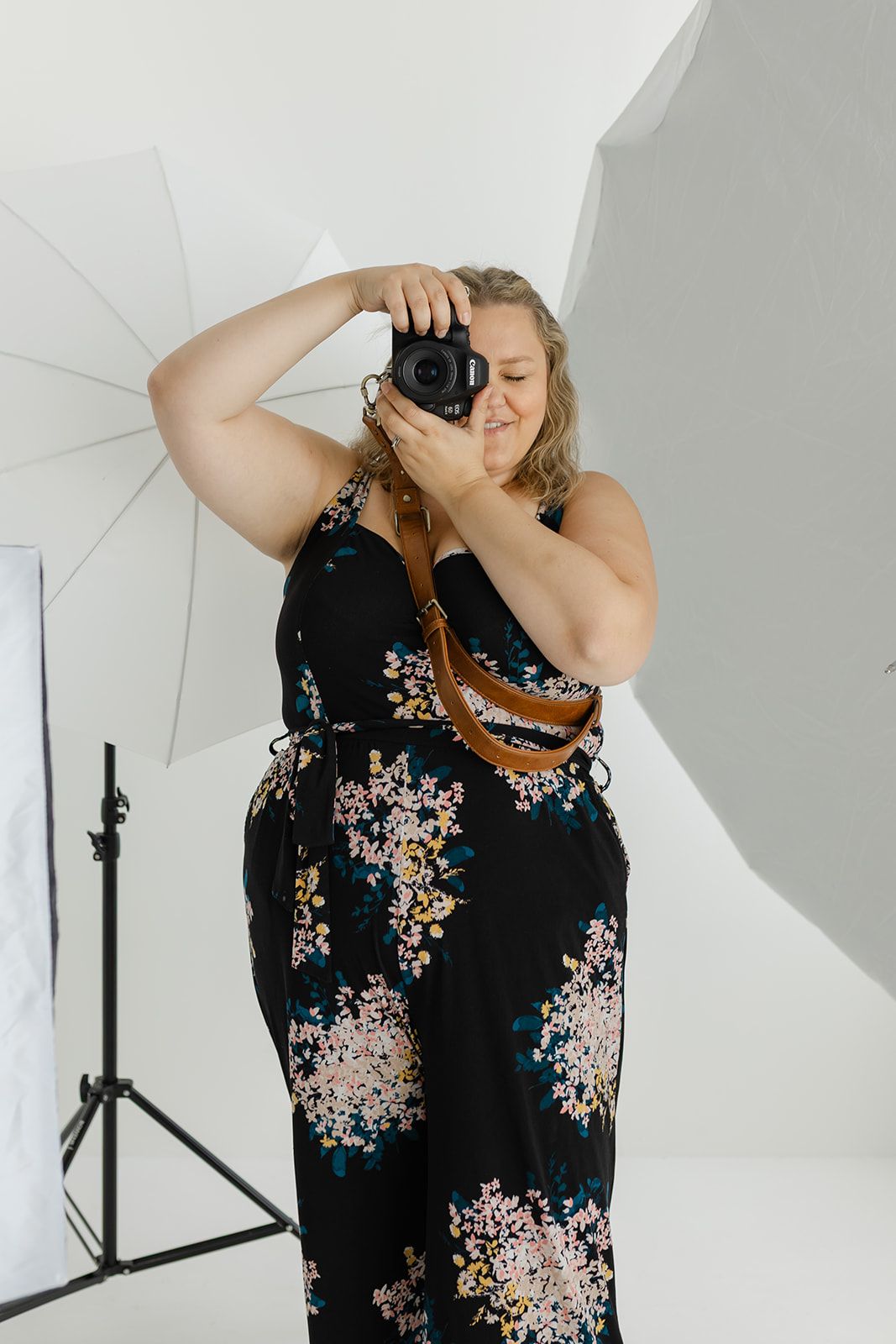 A woman holding a camera and taking a photograph in a studio setting.