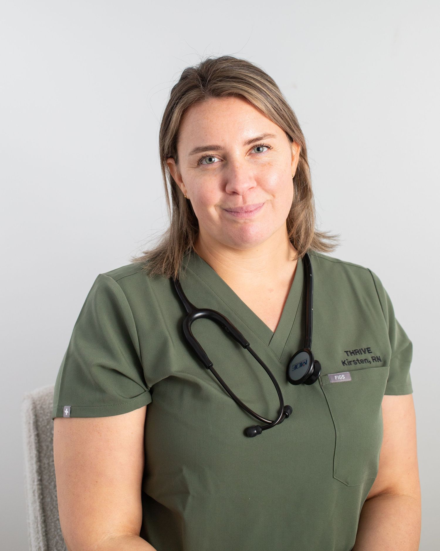 The image shows a smiling woman wearing a green medical uniform with a stethoscope around her neck.