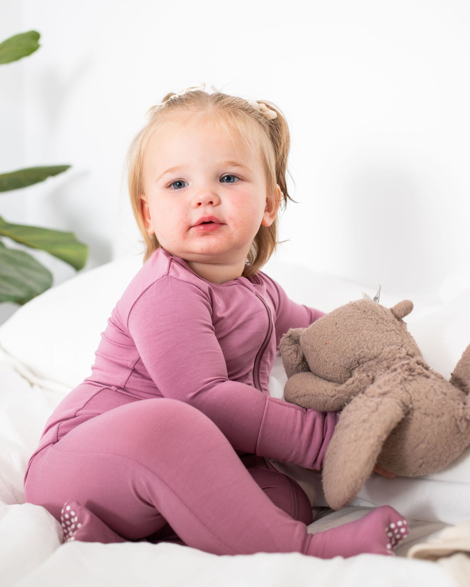 A smiling young girl in a pink outfit sitting on a white background and holding a stuffed animal.