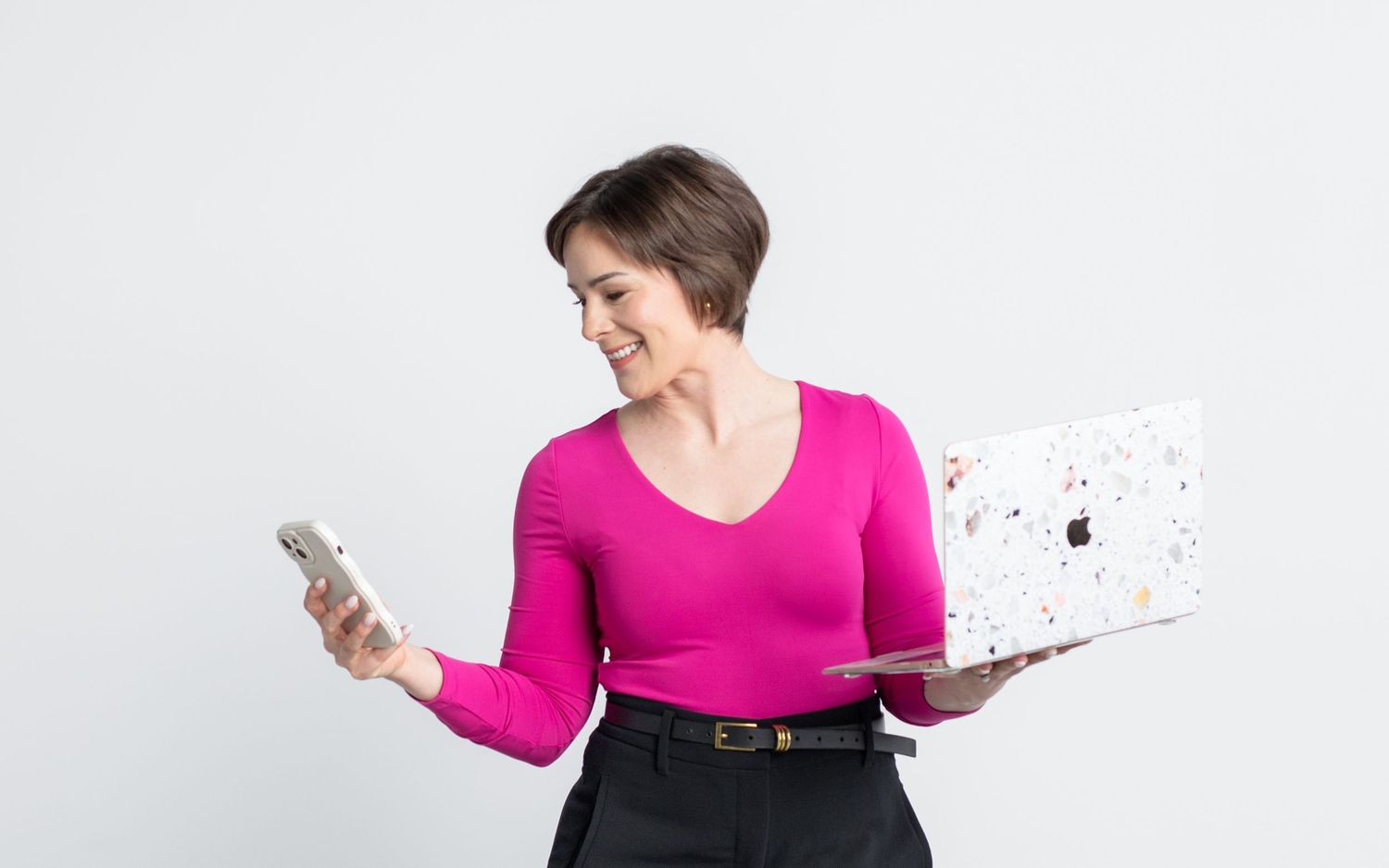 A woman in a pink top is holding a laptop and a smartphone.