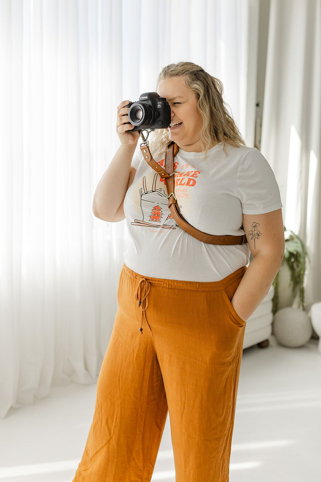 A woman holds a camera and takes a photograph, standing in a bright, open room.