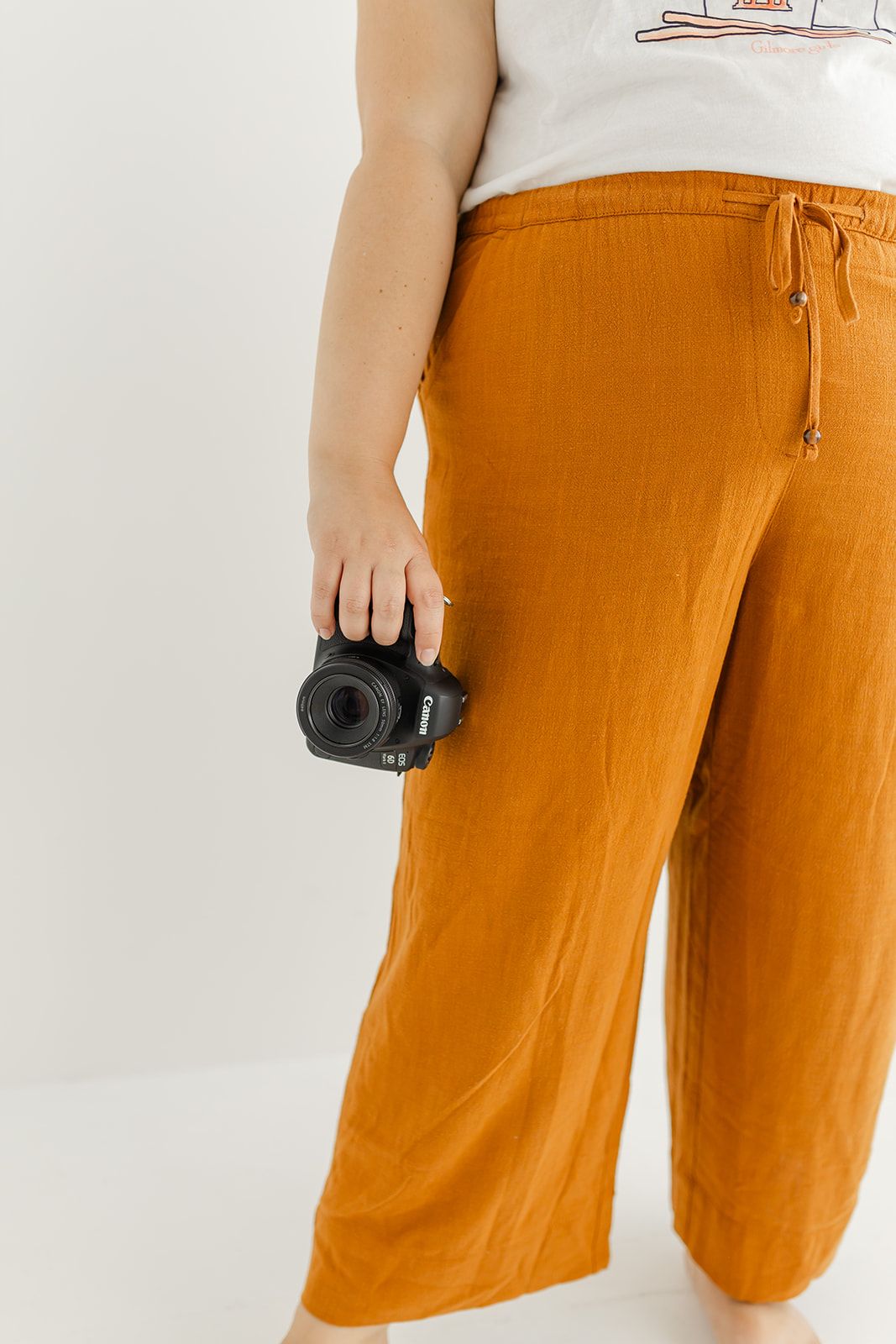 The image shows a person's lower body wearing orange drawstring pants and holding a camera in their hand.