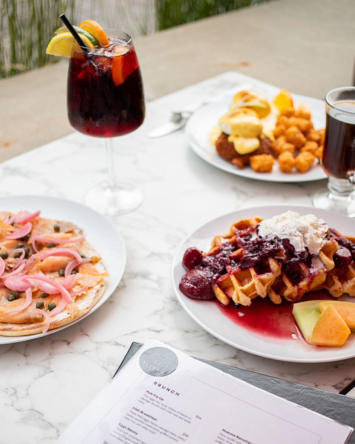 The image shows a table with various food items, including a cocktail, waffles, and a plate of food.
