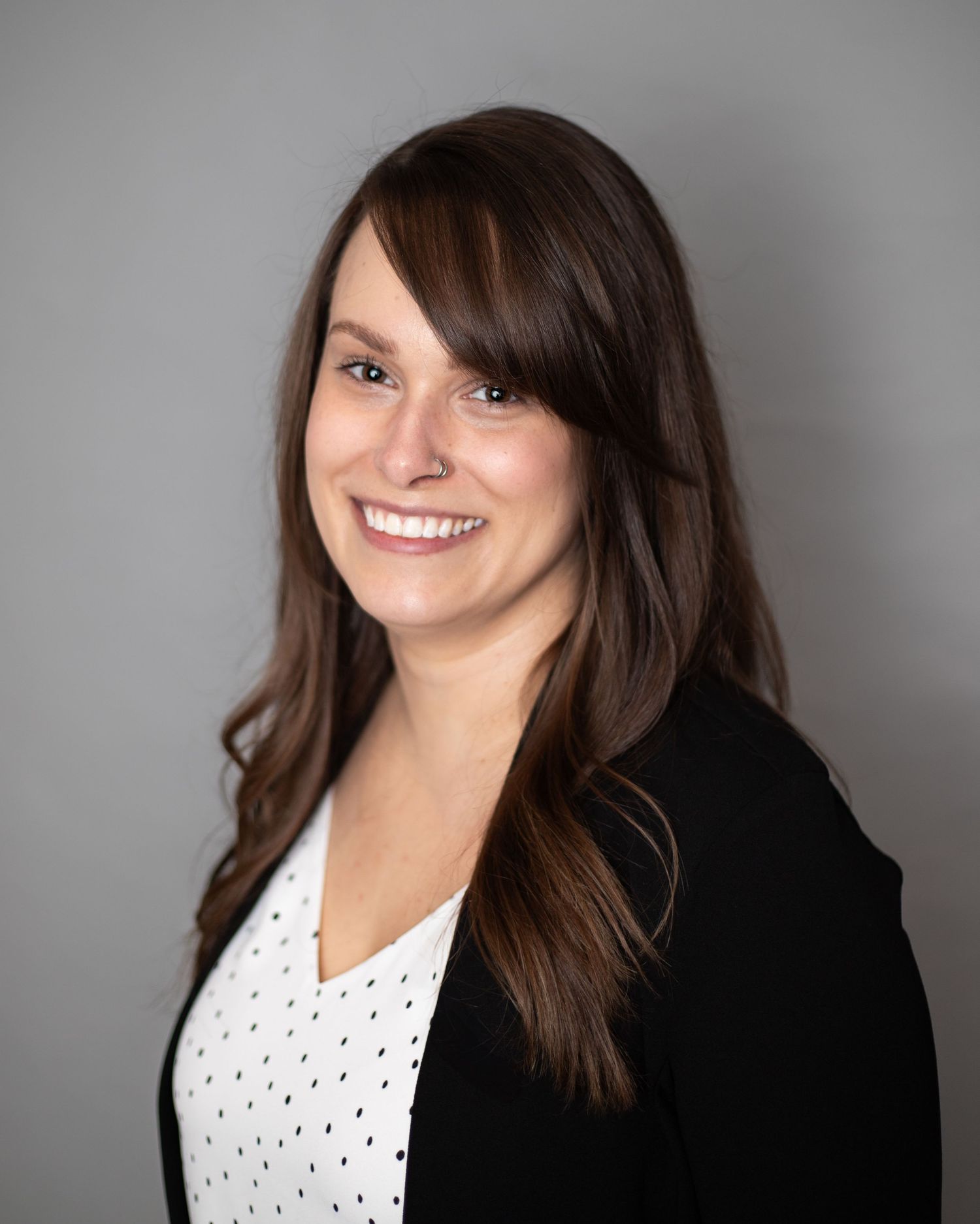 The image shows a smiling woman with long brown hair wearing a black top against a white background.