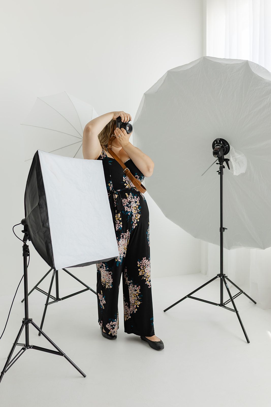 A woman poses for a photograph, surrounded by photography equipment in a bright, white studio.