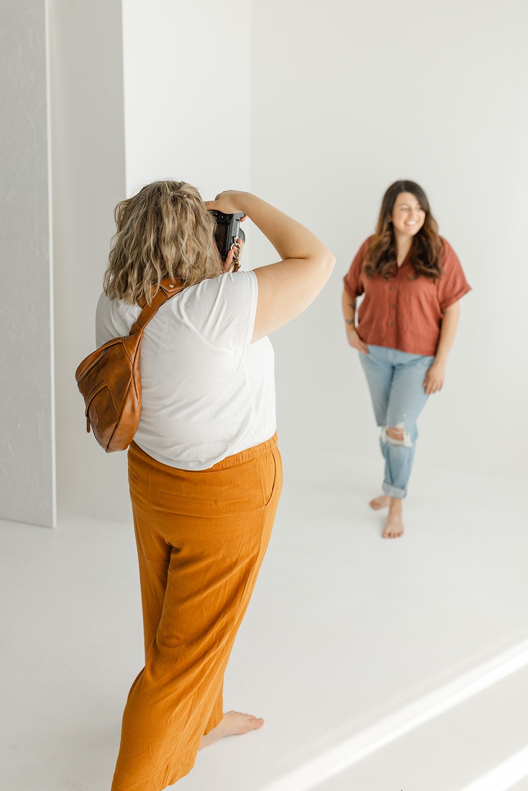 Image of a woman standing in a room, holding a camera and smiling.