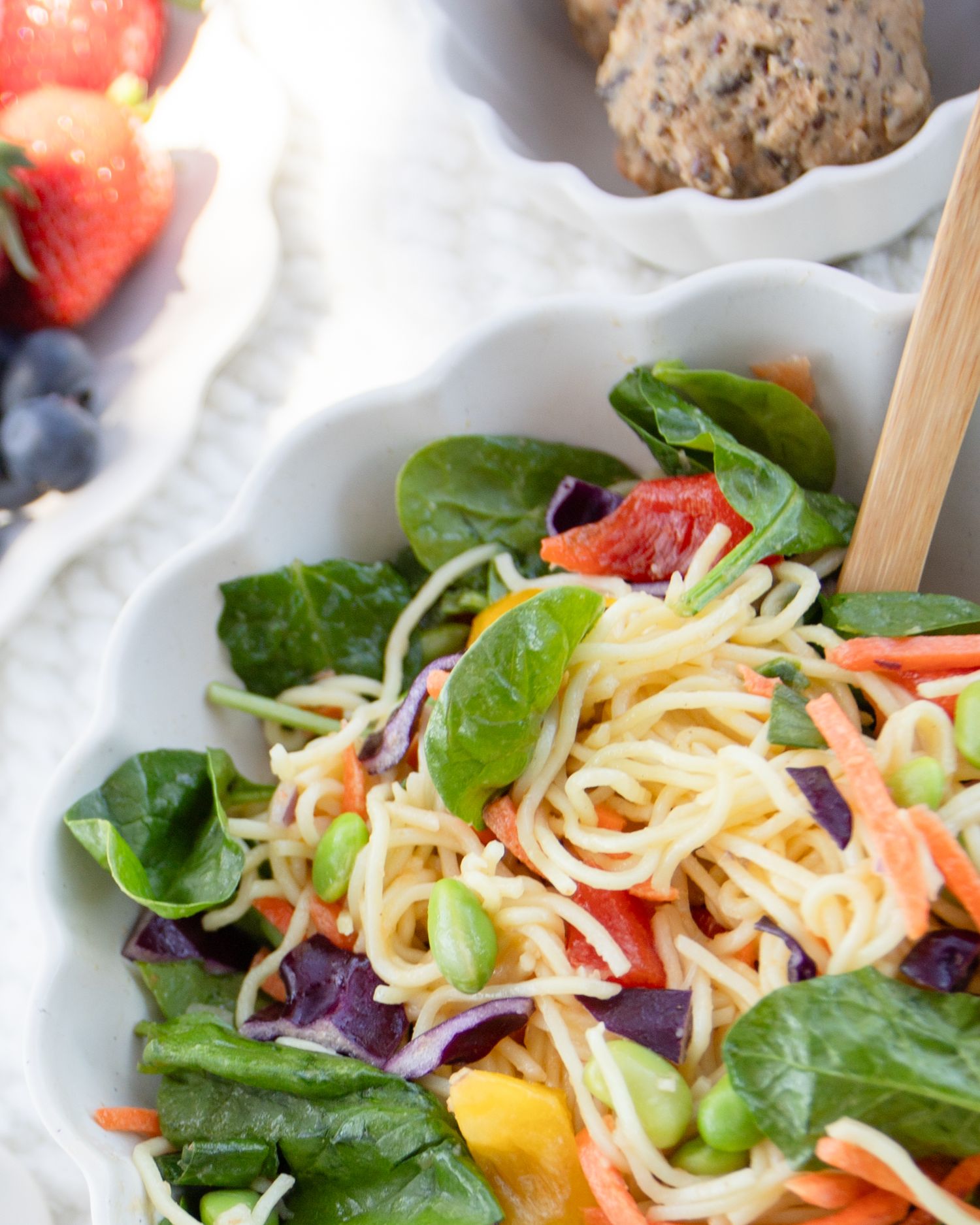 A salad with leafy greens, noodles, and various vegetables is displayed on a white plate.