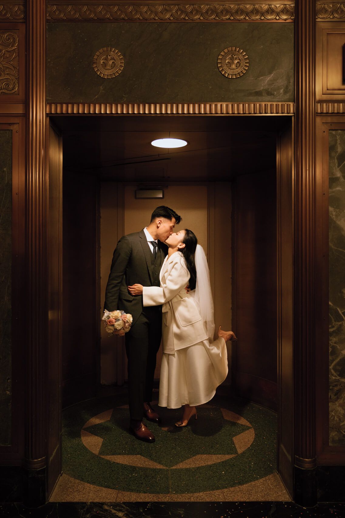 A bride and groom share a timeless kiss in Manhattan city hall; the bride, in a white outfit with veil and the groom in a dark suit