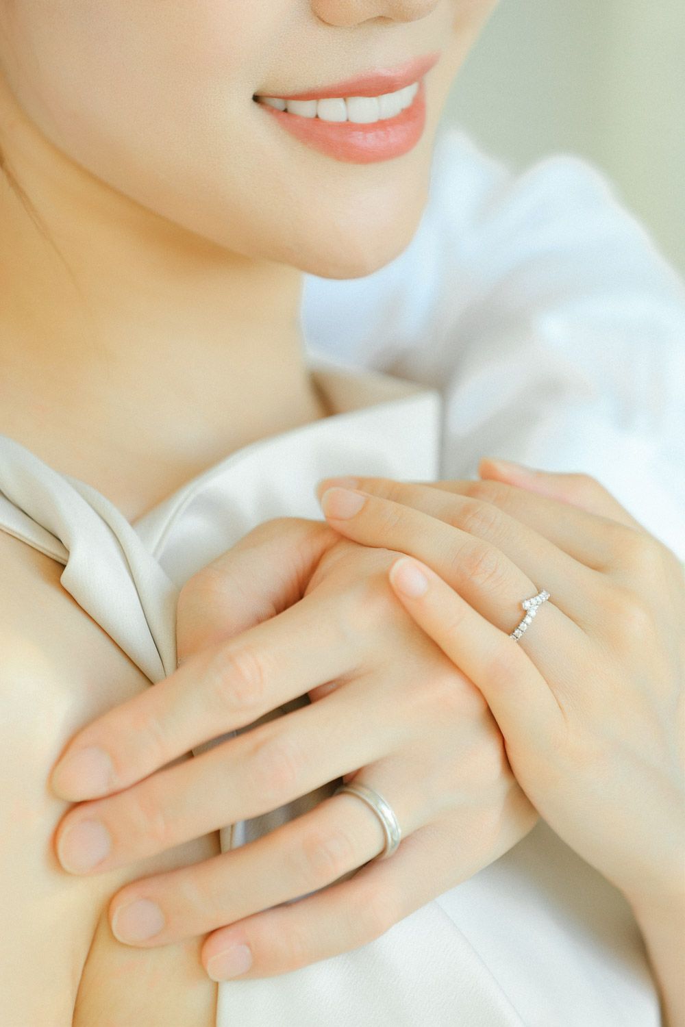 Close-up of a bride-to-be smiling with her hands gently clasped, showcasing her diamond engagement ring in timeless natural style.