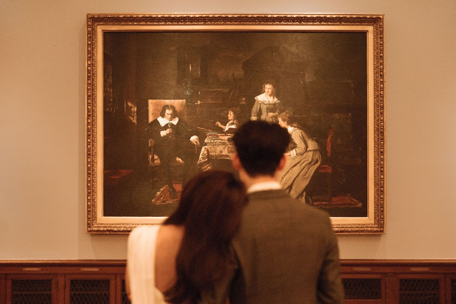 Cinematic back-view wedding portrait of a modern couple standing in the New York Public Library, looking at a large historical painting.