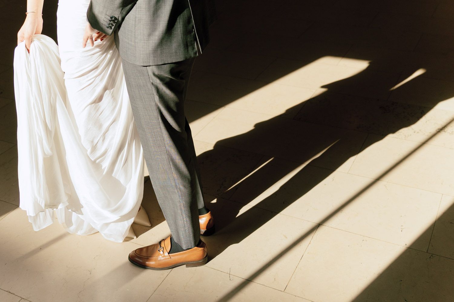 A couple stands together in dramatic natural light with long shadows on the floor during their timeless New York engagement at NYPL.
