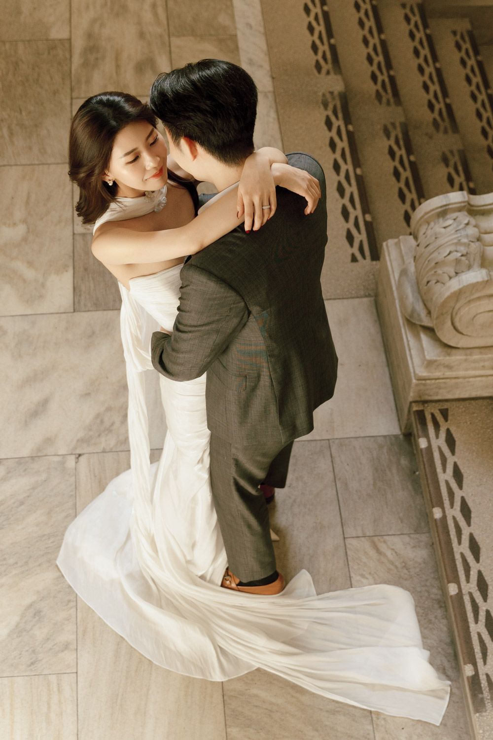 A romantic couple shares a tender embrace on grand marble stairs during their New York engagement session in timeless natural style at NYPL.