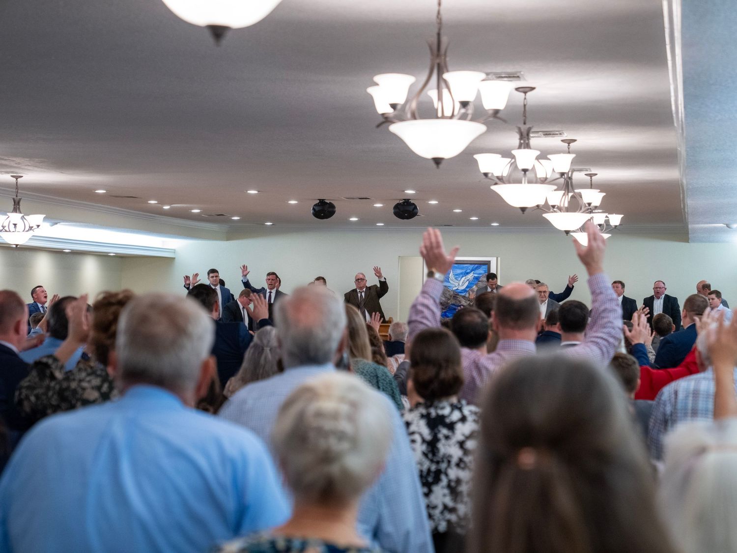 Large church congregation raising hands in praise during a worship service.