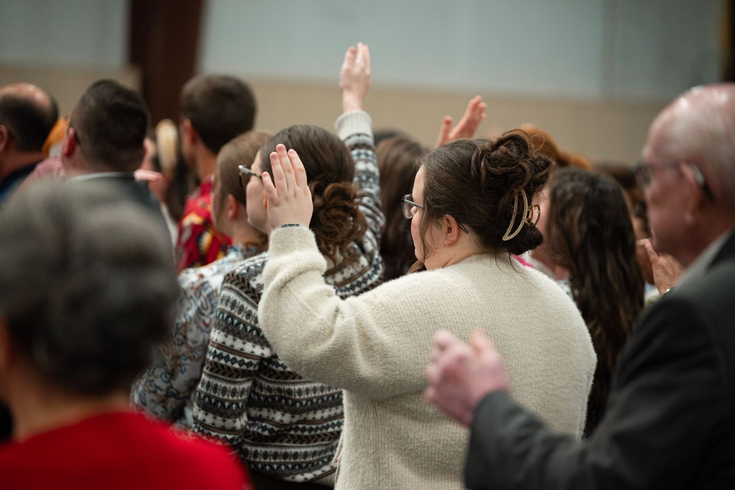 A woman raises her hand in prayer while standing among a congregation during a church service.