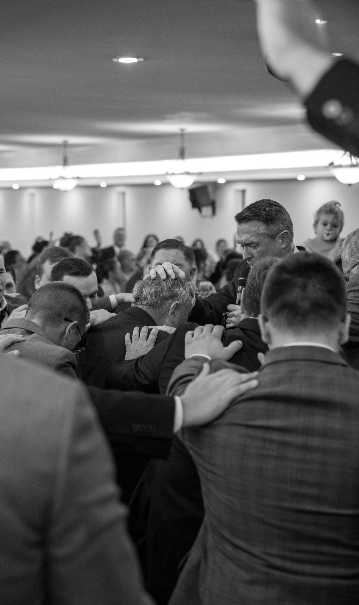 Black and white image of men laying hands in prayer on a congregant during a church service.