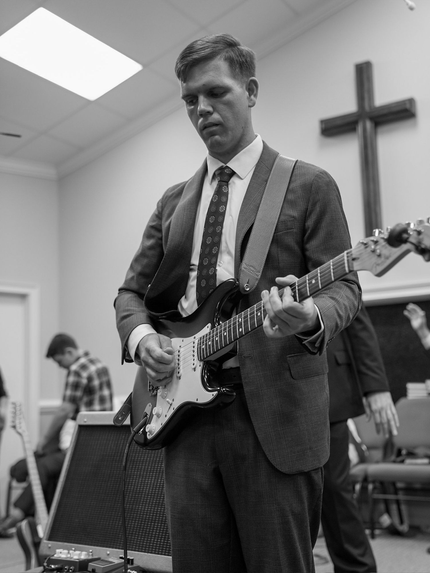 Young man in suit playing electric guitar during black and white church service.
