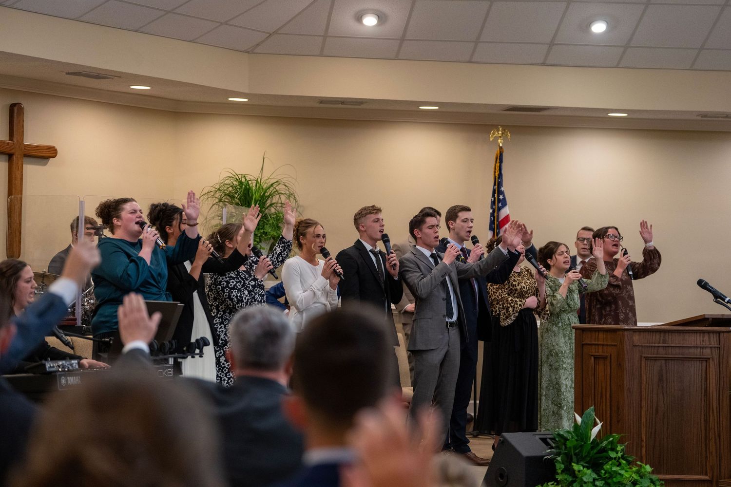 Congregation and choir raising hands in praise during a church worship service near an American flag.