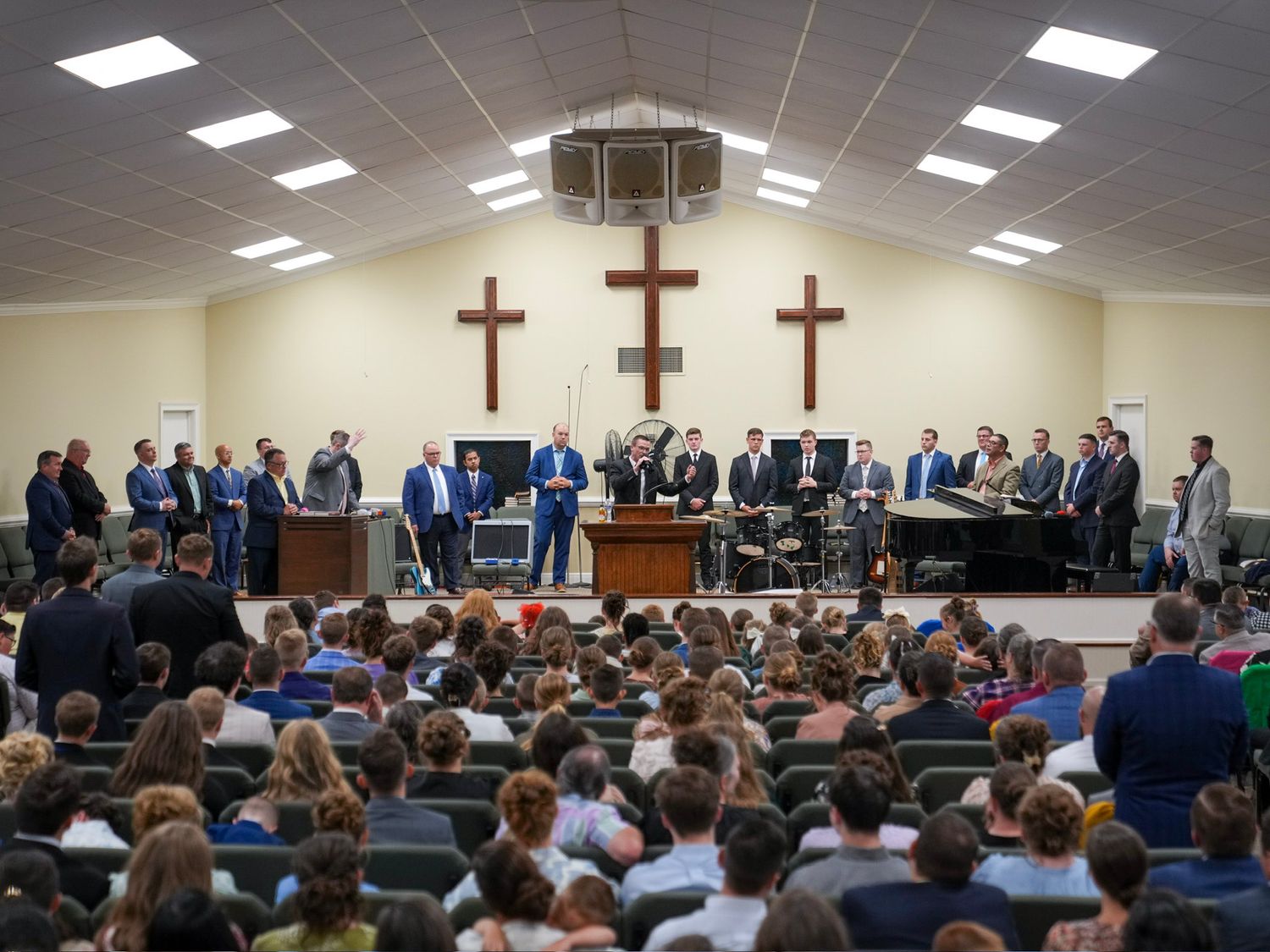 Large church congregation faces pastors and worship team standing before two wooden crosses on stage.