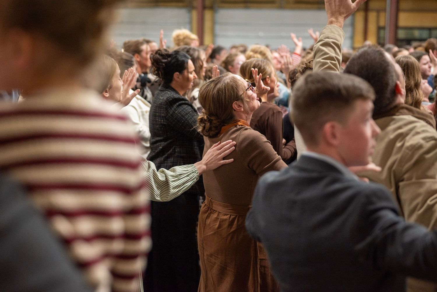 A congregation of worshippers embraces and raises hands during an emotional church revival service.