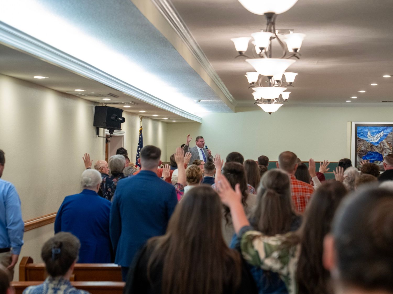 Pastor leading a standing congregation in worship inside a bright church sanctuary.