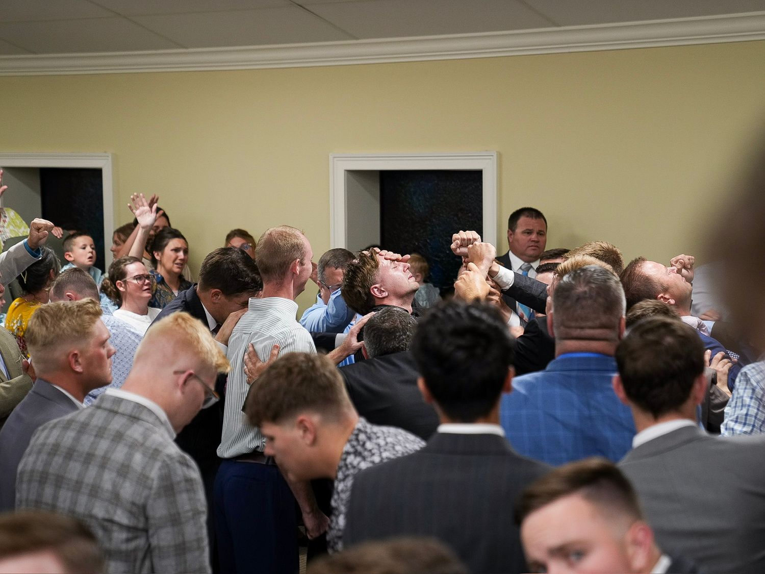 Group of men gathered in fervent prayer with raised hands during a church revival meeting.