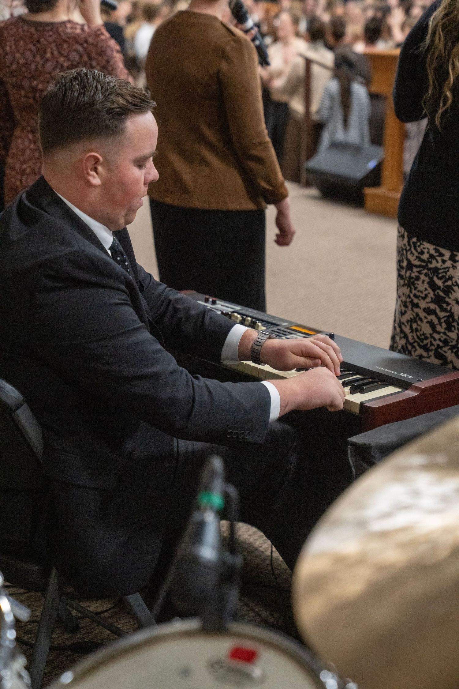 A young man in a suit plays a keyboard instrument during a live church worship service.