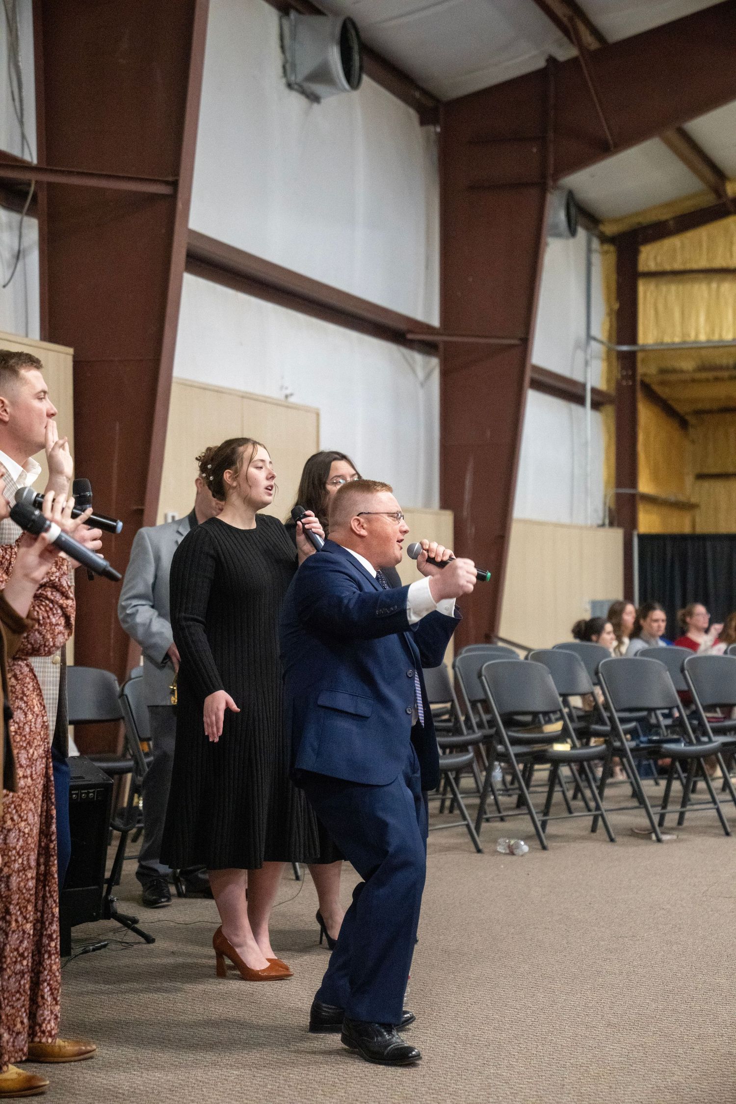 A worship team leads praise and worship with microphones in a large church event venue.