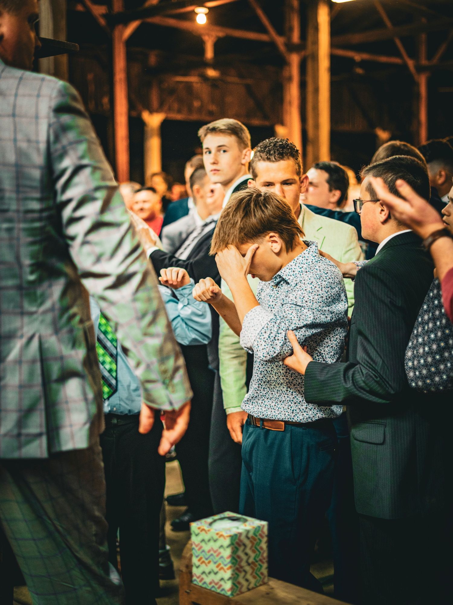 Young boy bowing head in emotional prayer during a church service in a rustic barn venue.