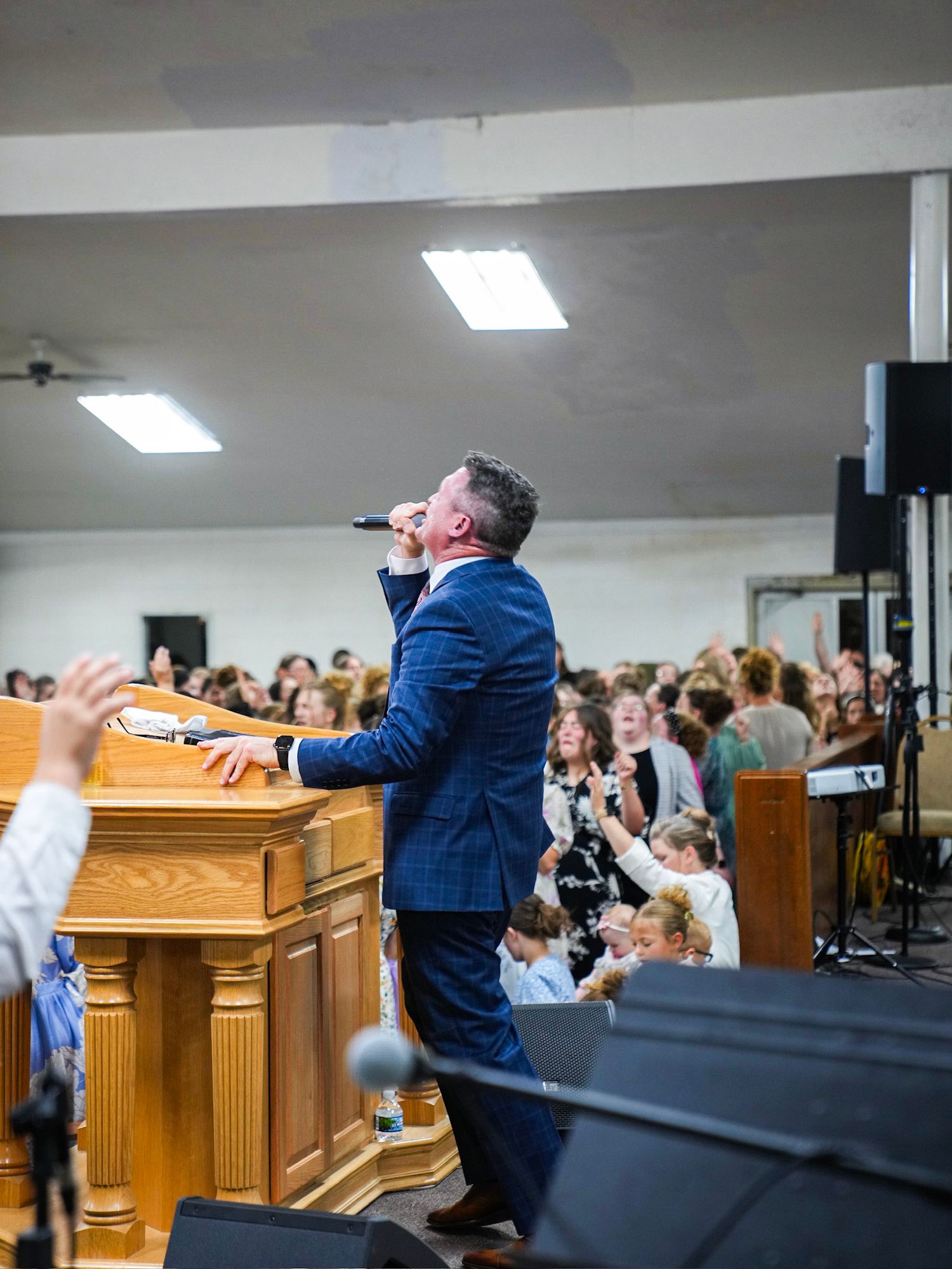 A pastor in a blue suit sings into a microphone before an engaged church congregation.