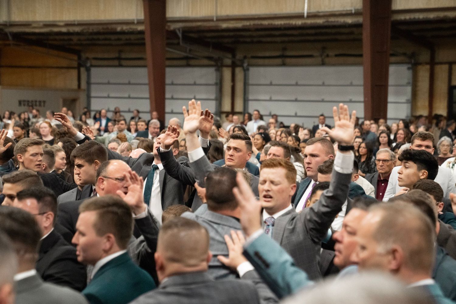 Large crowd of men in suits raising hands in worship at an indoor church conference event.