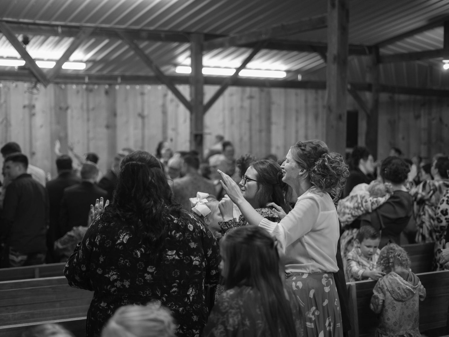 Black and white photo of worshippers raising hands in a rustic barn church setting.