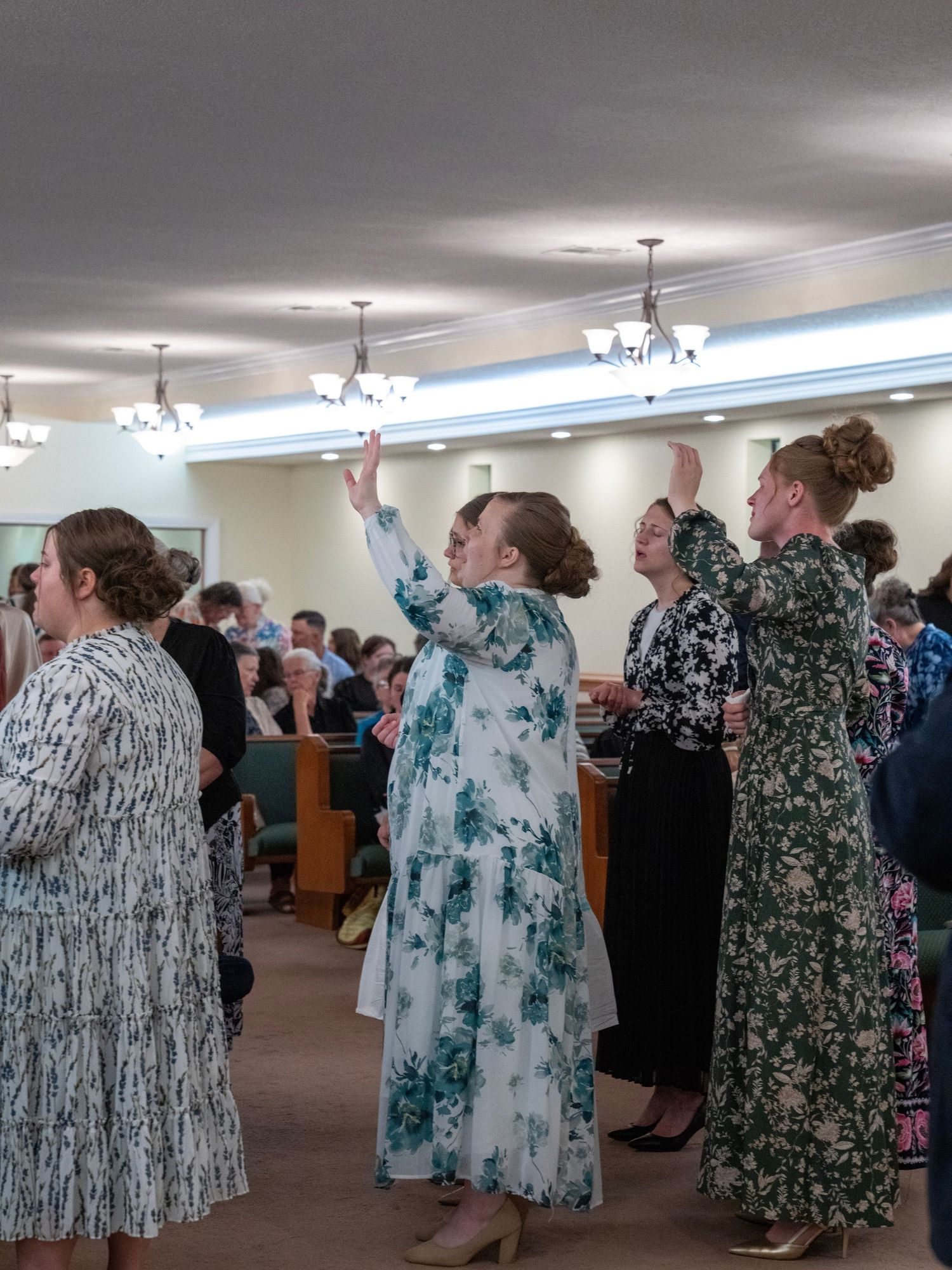 Women in floral dresses raising hands in worship during a church service.