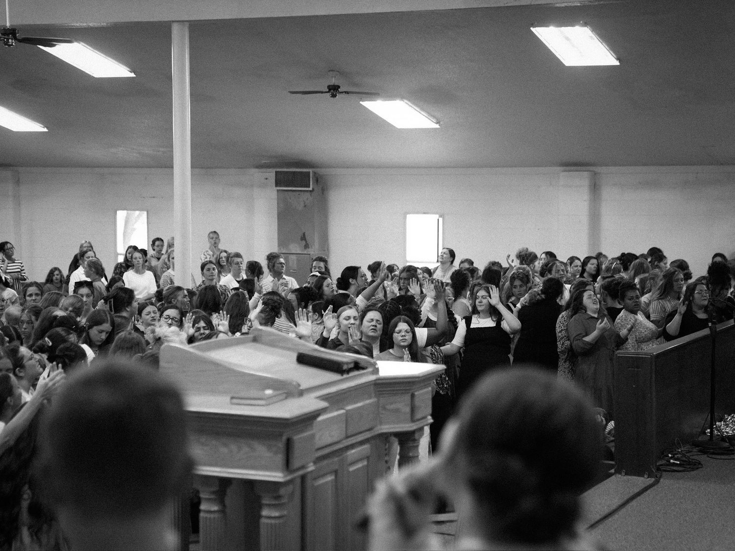 Black and white wide-angle view of a full congregation worshipping in a small church.