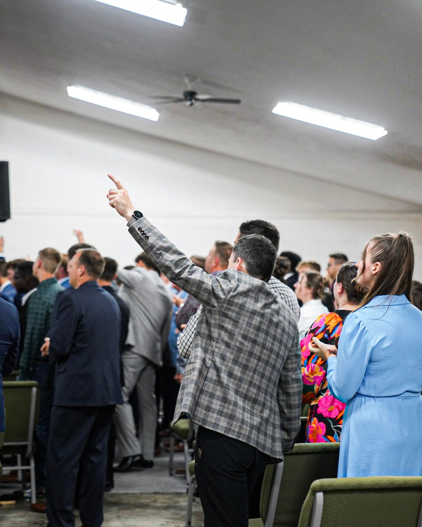 Man points upward in praise during a crowded church worship service.