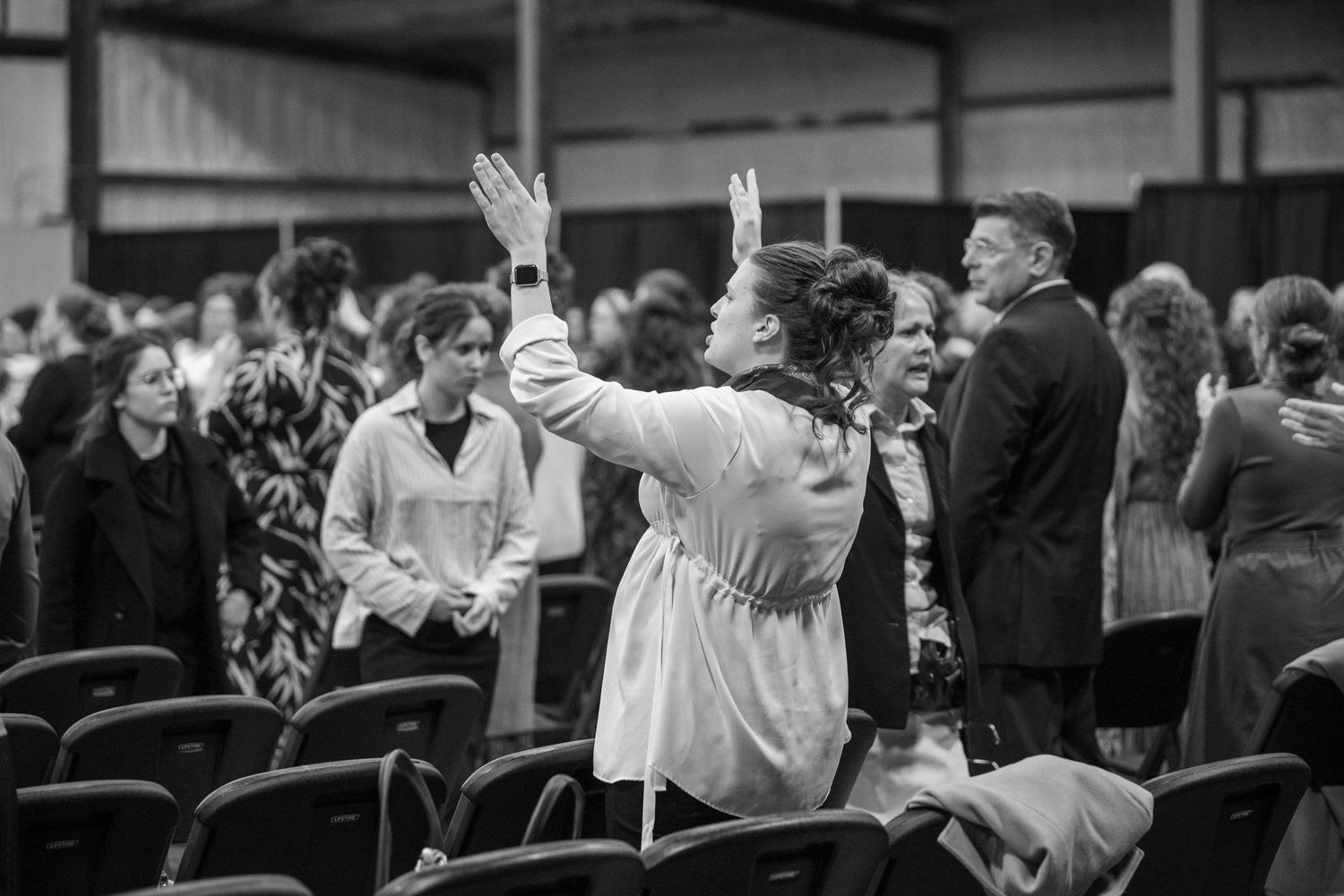 Black and white photo of a woman raising both hands in worship at a large church event.
