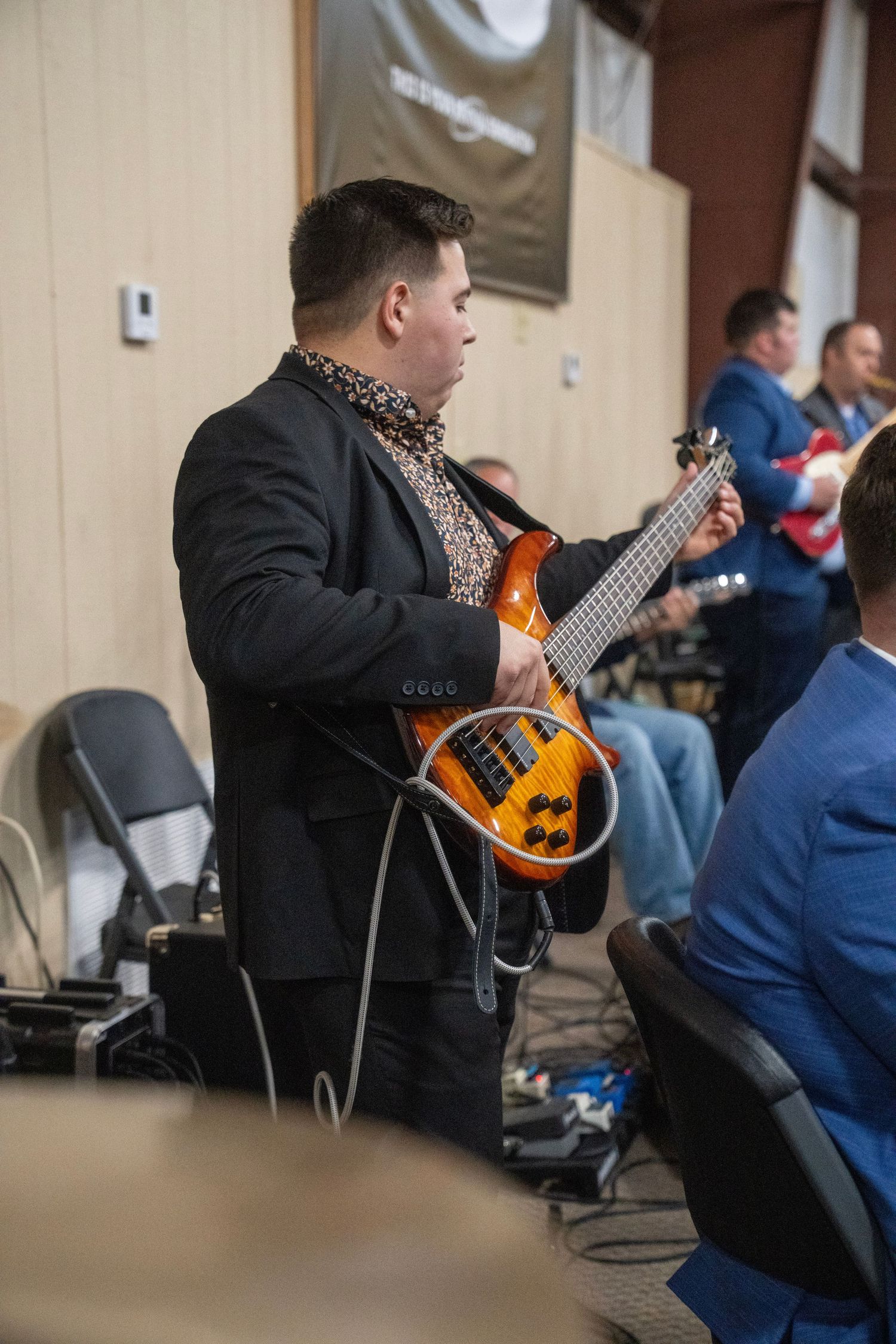 A guitarist in a black blazer plays an electric bass guitar during a live church worship service.