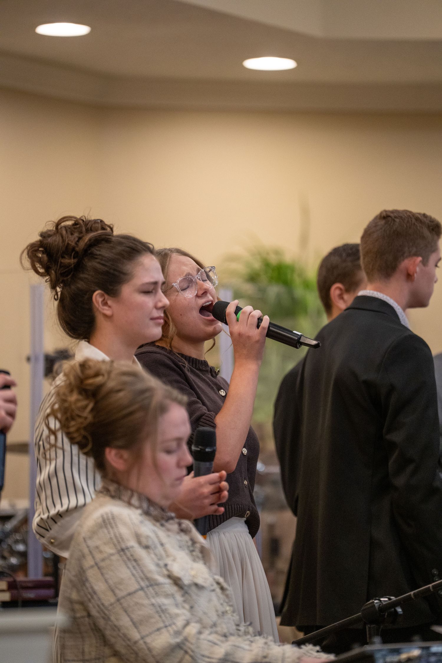 Young woman singing passionately into a microphone during a church worship service with musicians nearby.