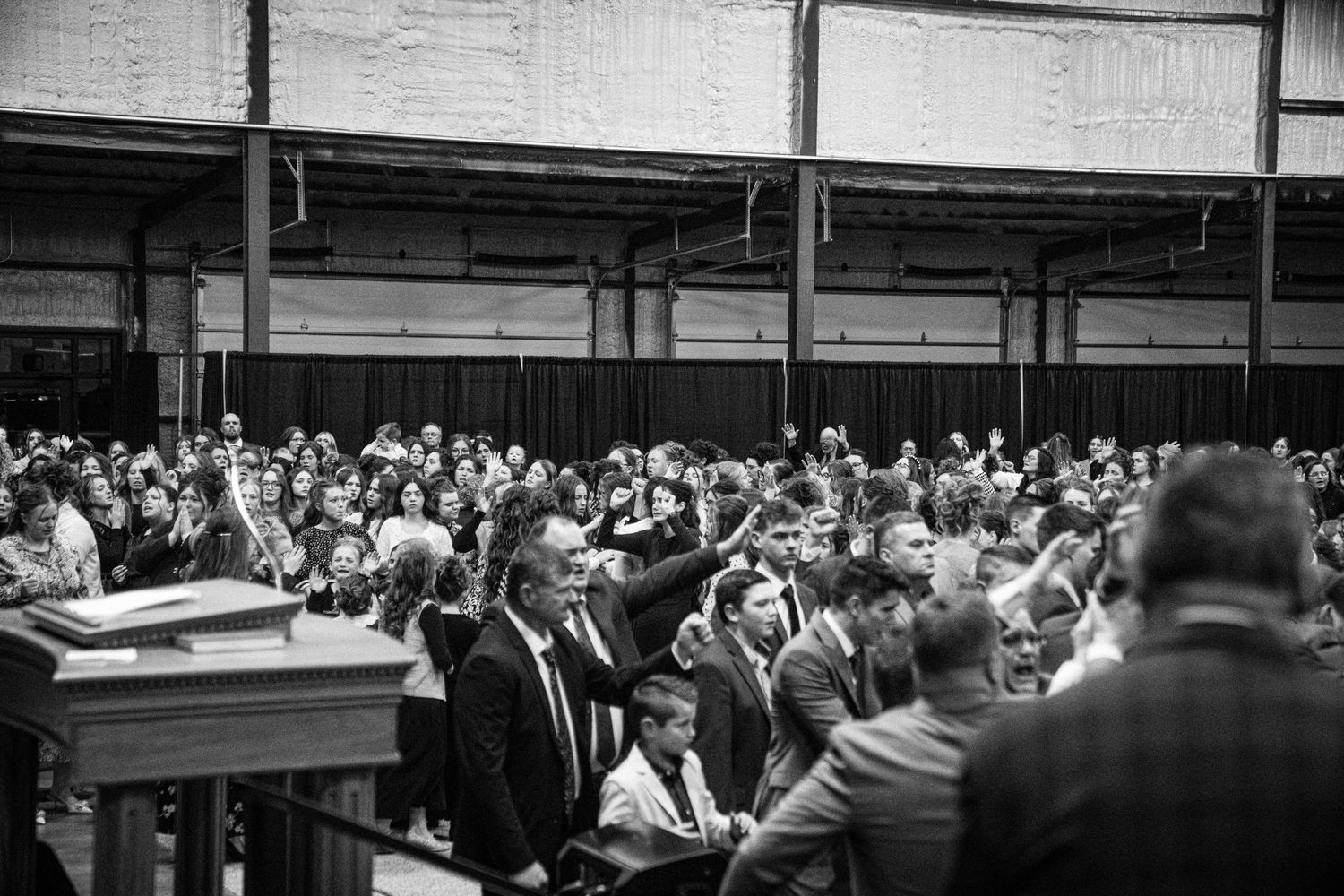 Black and white photo of a large congregation raising hands in worship during a church revival meeting.