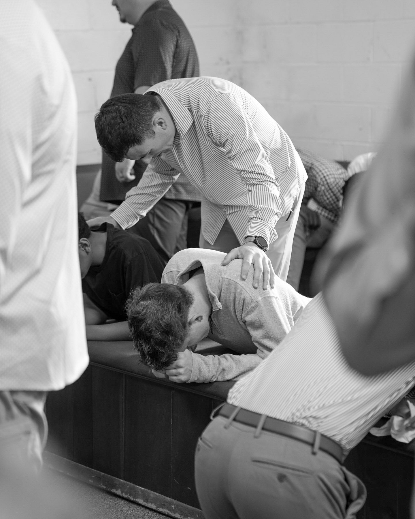 Man praying over a person kneeling at a church pew in black and white.