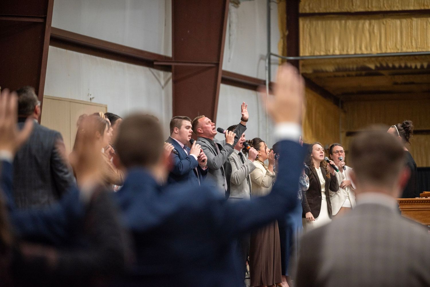 Congregation members in suits raise their hands in praise during an indoor worship service.
