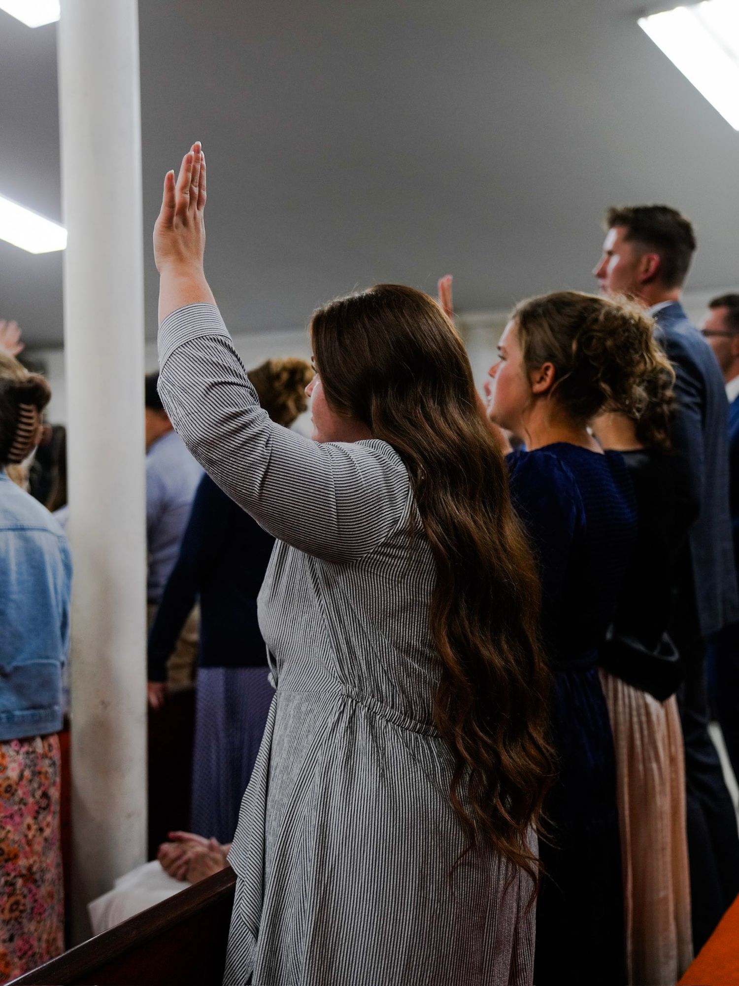 A young woman with long hair raises her hand in worship during a church service.