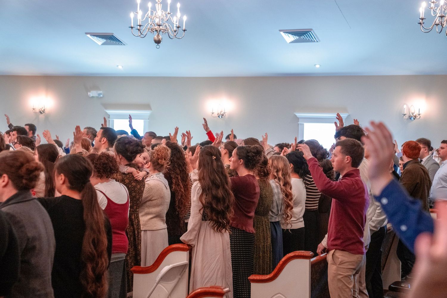 Large group of church congregation raising hands in praise during worship service.