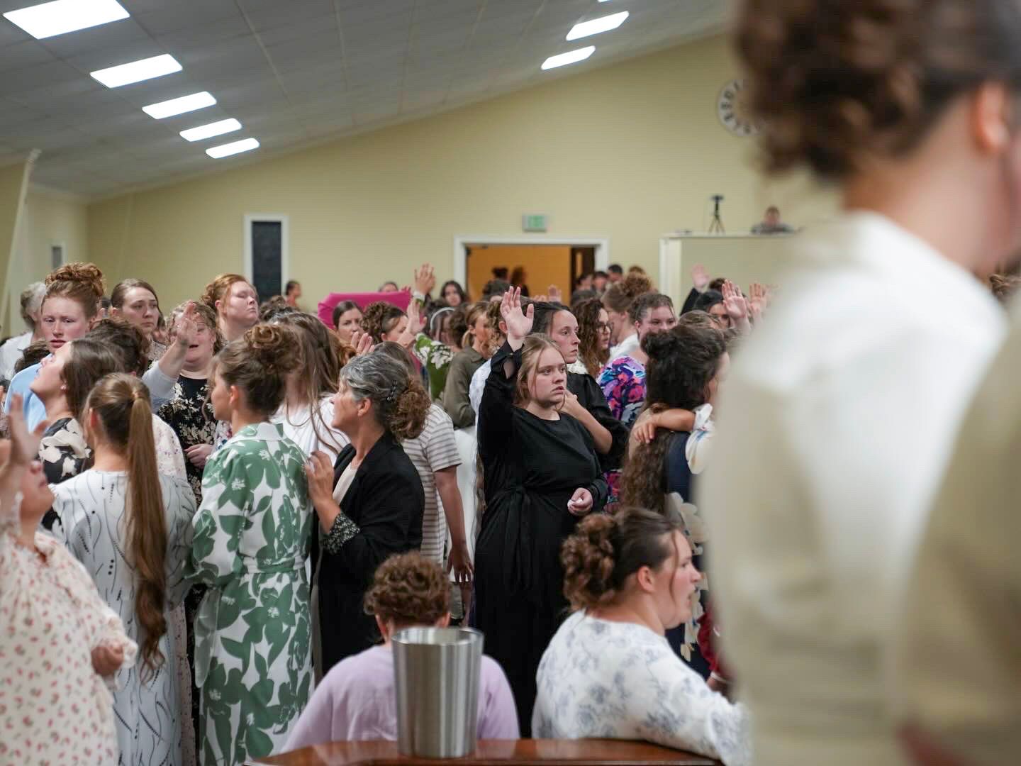 Women raising hands in heartfelt worship during a church revival service in a bright hall.