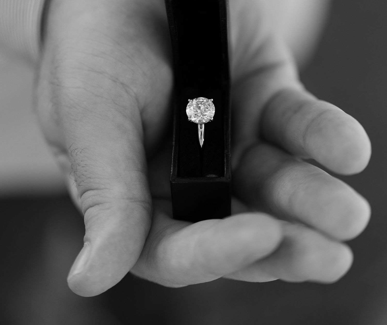 Black and white photo of hands holding a diamond engagement ring in a box.