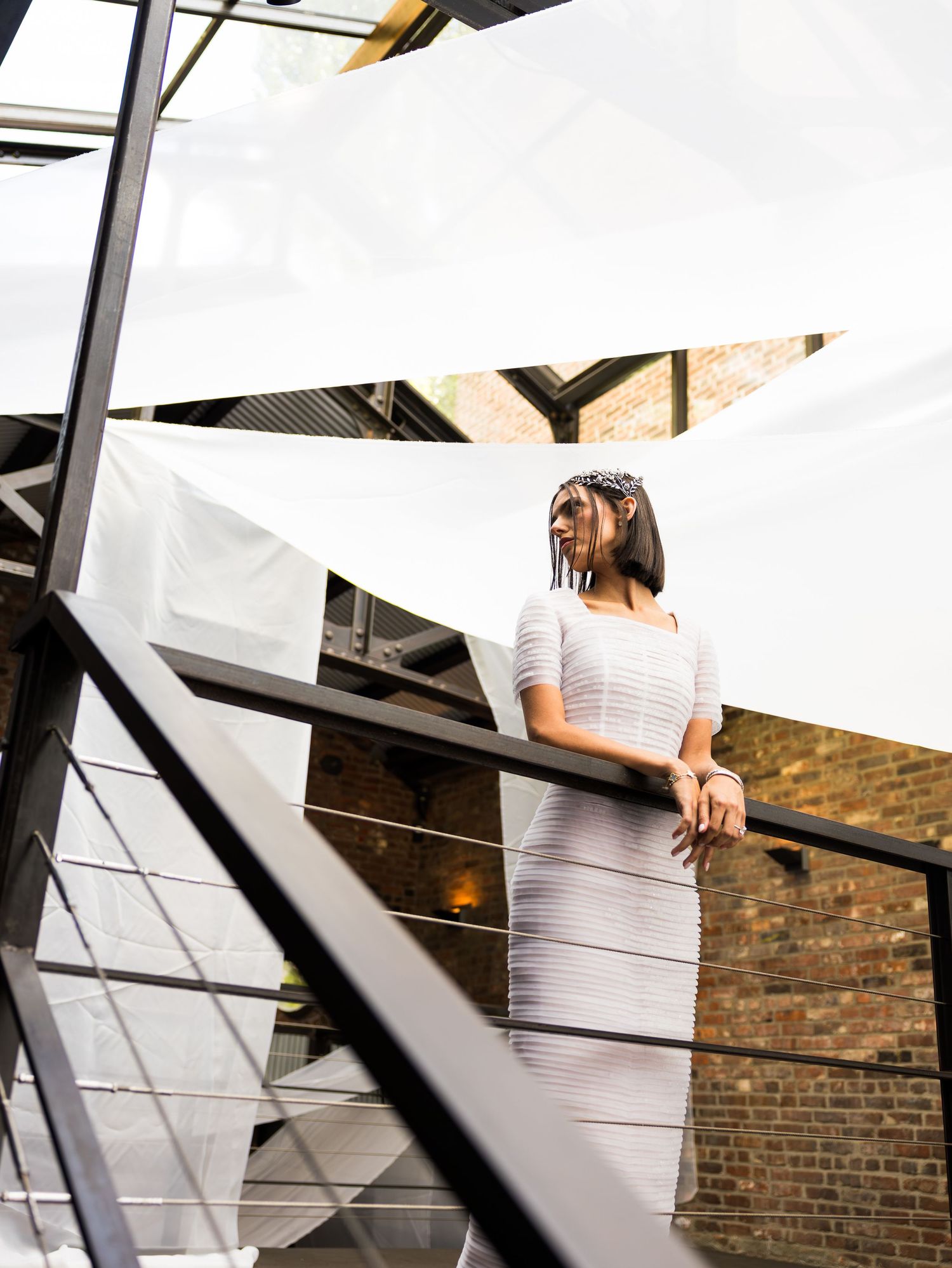 Bride in white fitted dress standing on industrial balcony with brick backdrop in the Foundry, Long Island City.
