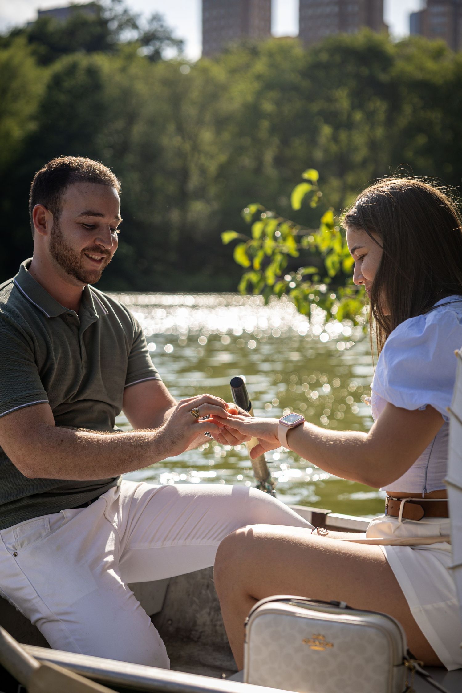 Man proposing to woman with ring box on a romantic boat ride on a sunlit lake in Central Park.