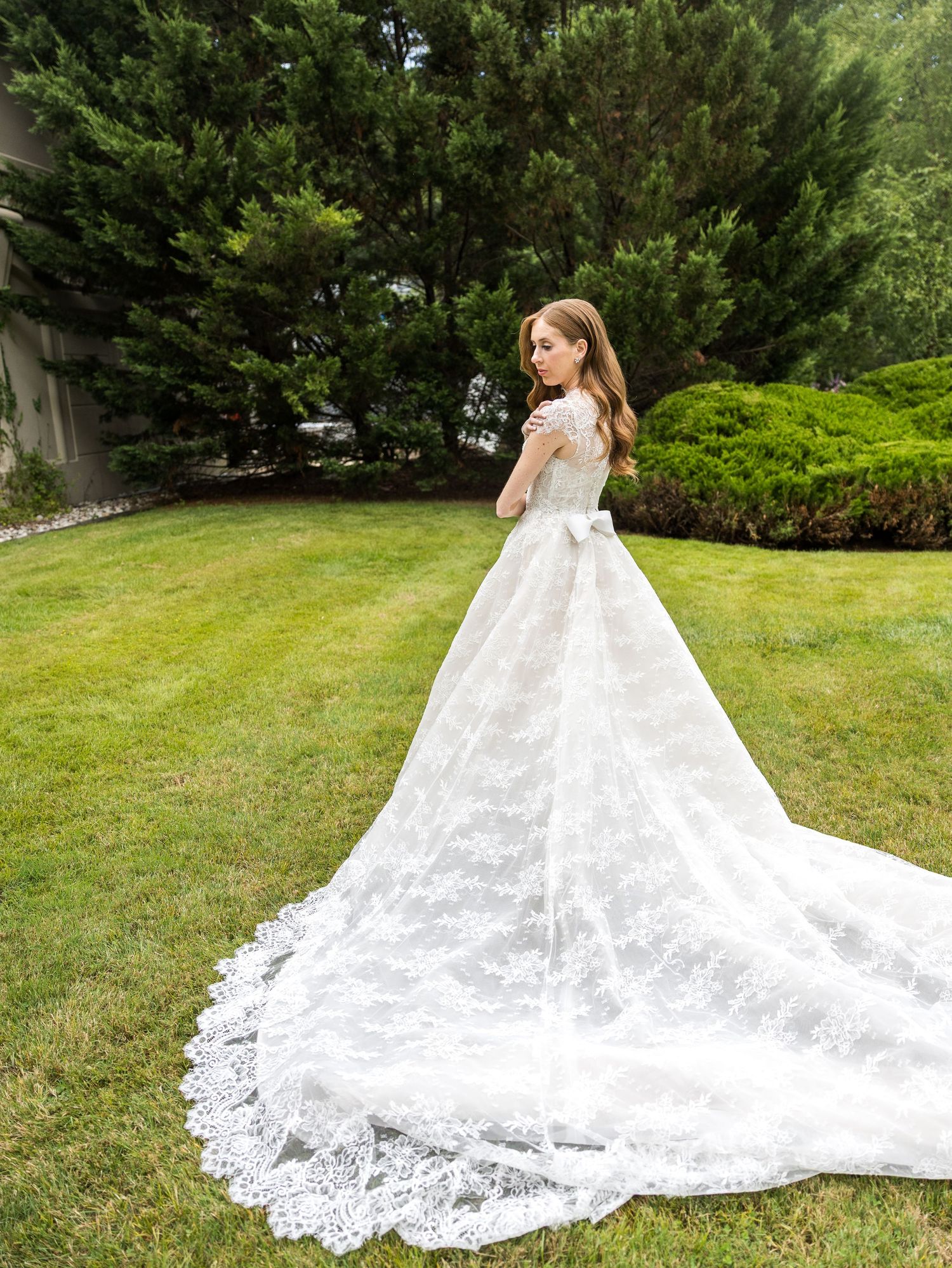 Bride in stunning lace ball gown with long train posing in garden setting In New Jersey.