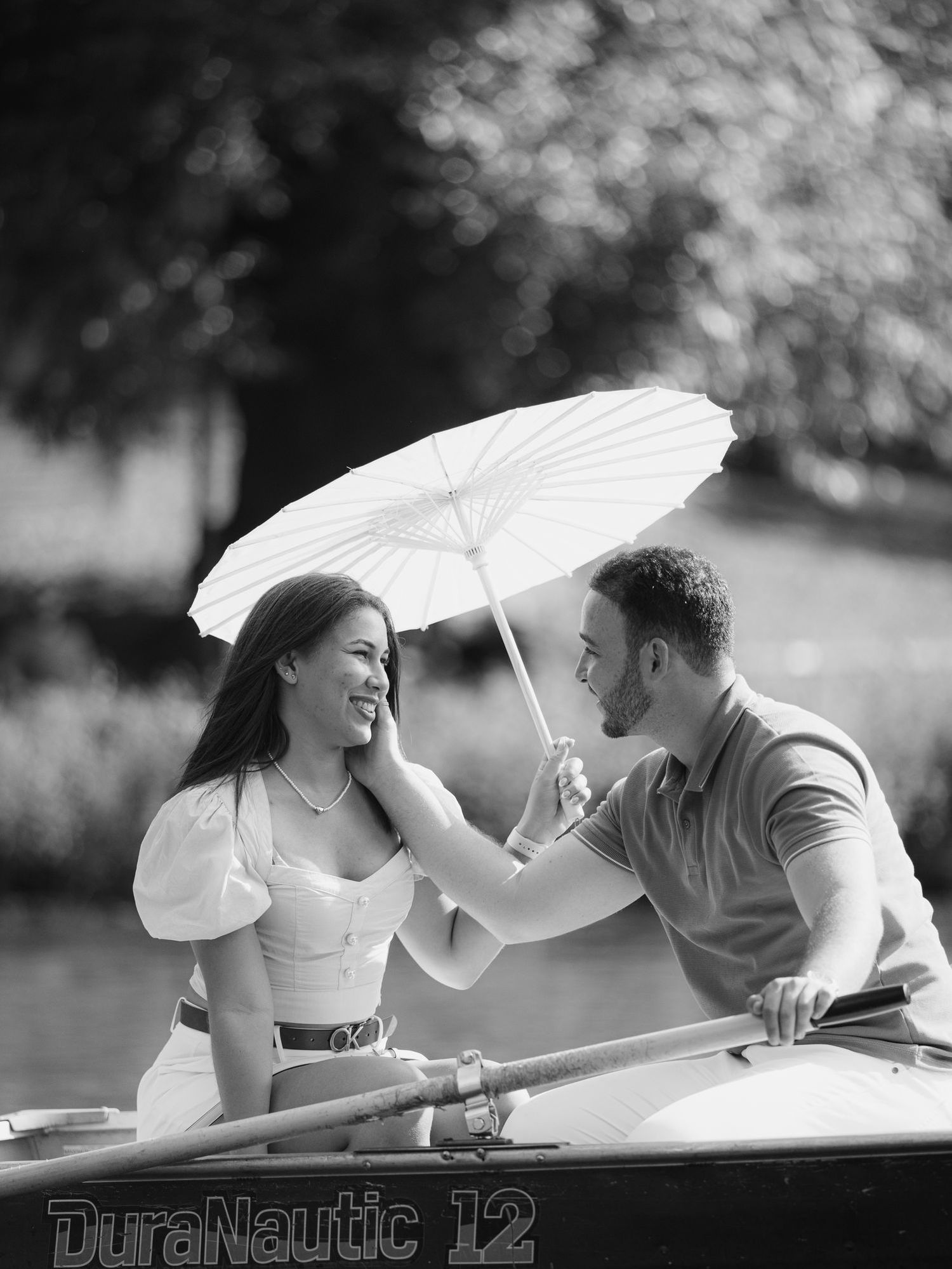 Black and white photo of a couple sharing a romantic moment on a boat under a white parasol umbrella.