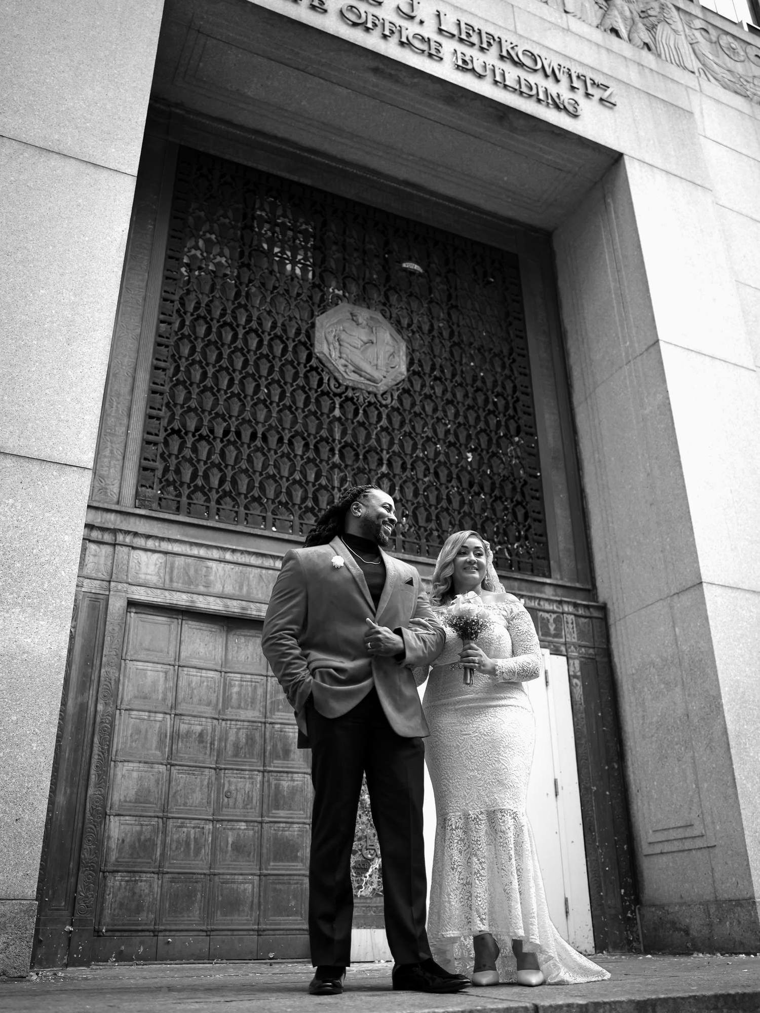 Black and white photo of a couple in wedding attire standing outside the Louis J. Lefkowitz State Office Building.